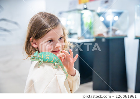 Little girl holding a green chameleon in her hands. Concept of childhood curiosity, interaction with exotic animals, and early interest in biology 126061961