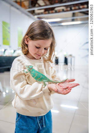 Little girl holding a green chameleon in her hands. Concept of childhood curiosity, interaction with exotic animals, and early interest in biology Little girl holding a green chameleon in her hands. Concept of childhood curiosity, interaction with exotic animals, and early interest in biology 126061963