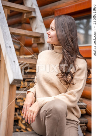 Young woman sitting on wooden stairs in a rustic countryside setting with firewood and tools in the background. Concept of rural lifestyle and simplicity of village life 126061966