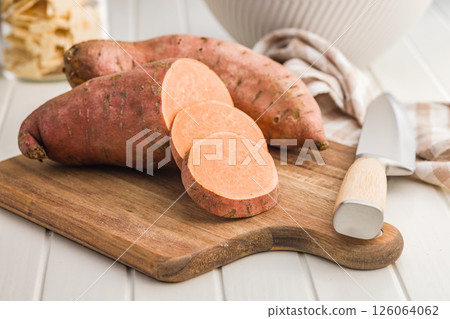 Raw sweet potatoes on cutting board on white table. 126064062