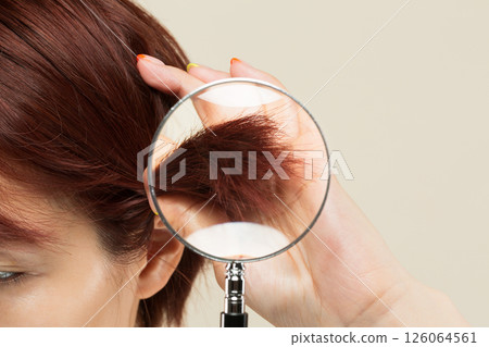 The ends of a woman's hair are magnified with a magnifying glass. 126064561