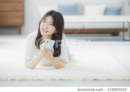 A woman lying down and looking at her smartphone A woman lying down and looking at her smartphone 126065025