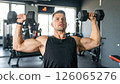 Athletic man performing shoulder press with dumbbells in modern gym, showcasing strength and focus 126065276