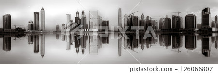 Monochrome city skyline with tall skyscrapers reflecting on calm water under a cloudy sky, Dubai Marina bay UAE Monochrome city skyline with tall skyscrapers reflecting on calm water under a cloudy sky, Dubai Marina bay UAE 126066807
