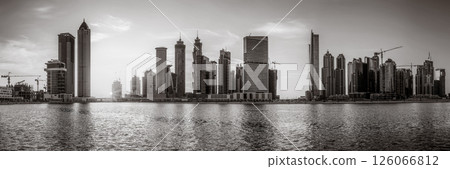 Monochrome city skyline with tall skyscrapers reflecting on calm water under a cloudy sky, Dubai Marina bay UAE Monochrome city skyline with tall skyscrapers reflecting on calm water under a cloudy sky, Dubai Marina bay UAE 126066812