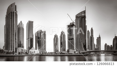 Monochrome city skyline with tall skyscrapers reflecting on calm water under a cloudy sky, Dubai Marina bay UAE 126066813