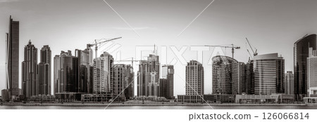 Monochrome city skyline with tall skyscrapers reflecting on calm water under a cloudy sky, Dubai Marina bay UAE 126066814