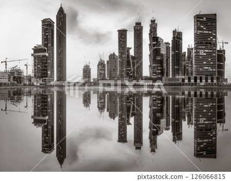 Monochrome city skyline with tall skyscrapers reflecting on calm water under a cloudy sky, Dubai Marina bay UAE Monochrome city skyline with tall skyscrapers reflecting on calm water under a cloudy sky, Dubai Marina bay UAE 126066815