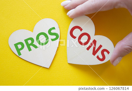 Pros vs Cons symbol. Concept word Pros vs Cons on wooden hearts. Businessman hand. Beautiful yellow background. Business and Pros vs Cons concept. Copy space 126067814