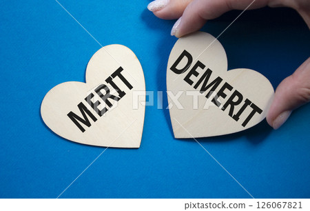 Merit or Demerit symbol. Concept word Merit or Demerit on wooden hearts. Businessman hand. Beautiful blue background. Business and Merit or Demerit concept. Copy space Merit or Demerit symbol. Concept word Merit or Demerit on wooden hearts. Businessman hand. Beautiful blue background. Business and Merit or Demerit concept. Copy space 126067821