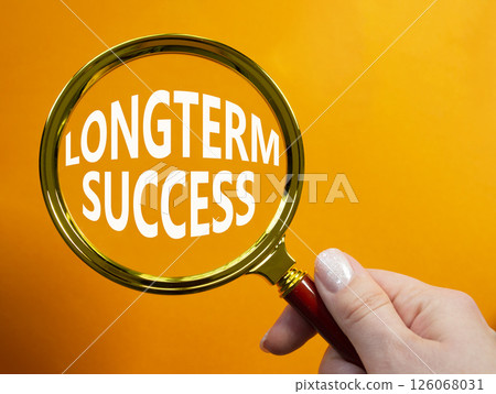 Longterm success symbol. Magnifying Glass with Concept word Longterm success. Businessman hand. Beautiful orange background. Business and Longterm success concept. Copy space 126068031