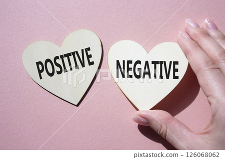 Positive or Negative symbol. Concept word Positive or Negative on wooden hearts. Businessman hand. Beautiful pink background. Business and Positive or Negative concept. Copy space Positive or Negative symbol. Concept word Positive or Negative on wooden hearts. Businessman hand. Beautiful pink background. Business and Positive or Negative concept. Copy space 126068062