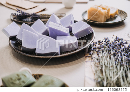 Close-up of handmade lavender soap bars arranged on a ceramic plate with dried lavender and green soap nearby. Aromatherapy, clean beauty, sustainable ingredients, botanical skincare Close-up of handmade lavender soap bars arranged on a ceramic plate with dried lavender and green soap nearby. Aromatherapy, clean beauty, sustainable ingredients, botanical skincare 126068255
