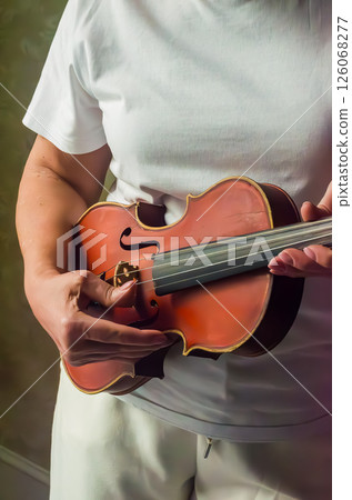 Person is holding a small violin with focused expression in softly lit indoor environment. High quality photo Person is holding a small violin with focused expression in softly lit indoor environment. High quality photo 126068277