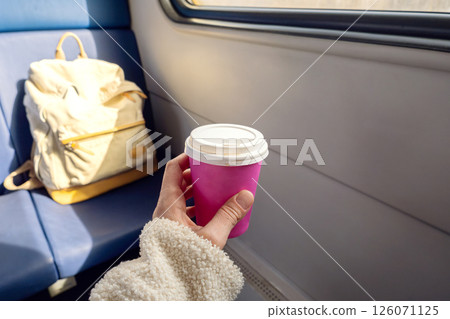 Woman Holding Disposable Coffee Cup on Train. Passenger Enjoying Hot Drink During SoloTravel Vacation or Daily Commute. 126071125