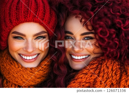Two smiling women, bundled in warm winter scarves and hats, share a joyful moment outdoors Two smiling women, bundled in warm winter scarves and hats, share a joyful moment outdoors 126071336