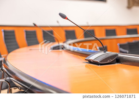 Microphones and round brown table in an empty conference room. Beginning of session meeting with black chair 126071871