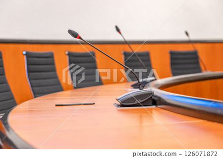 Microphones and round brown table in an empty conference room. Beginning of session meeting with black chair Microphones and round brown table in an empty conference room. Beginning of session meeting with black chair 126071872