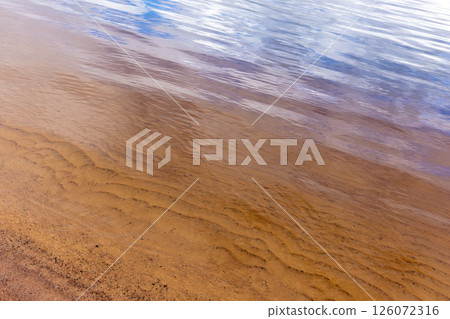 A tranquil scene of rippling water on a sandy shoreline 126072316