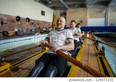 Focused forced rowing athletes train intensely on rowing simulator during synchronized team workout 126073156