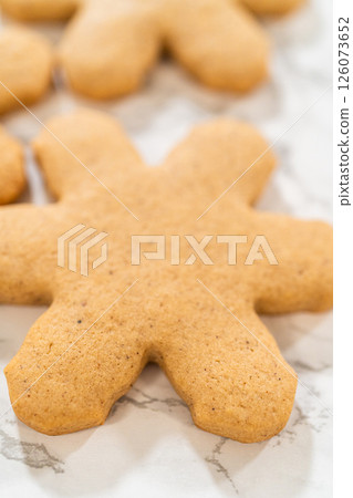Close-up side view of a hand holding a freshly baked snowflake-shaped amber gingerbread cookie with others arranged on a marble countertop, showcasing their golden-brown festive design. Close-up side view of a hand holding a freshly baked snowflake-shaped amber gingerbread cookie with others arranged on a marble countertop, showcasing their golden-brown festive design. 126073652