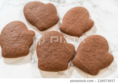Angled close-up of four Pale Gingerbread Cookies shaped like mittens, highlighting their festive details and rich brown color. Angled close-up of four Pale Gingerbread Cookies shaped like mittens, highlighting their festive details and rich brown color. 126073657
