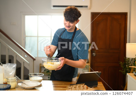 Cheerful man blending ingredients for pancakes, creating a homemade breakfast 126074407