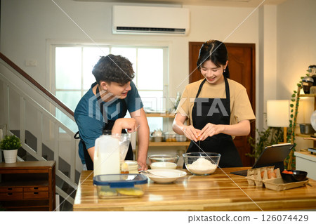 Happy couple cooking breakfast at home following digital recipe to make pancakes in a kitchen Happy couple cooking breakfast at home following digital recipe to make pancakes in a kitchen 126074429