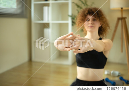 Fit young woman in sportswear doing arm stretches in a cozy home Fit young woman in sportswear doing arm stretches in a cozy home 126074436