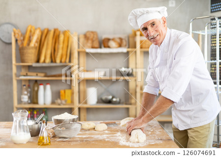 Elderly man baker rolls out dough 126074691