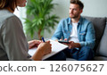 focused woman jotting down notes, man in thoughtful gaze during a serious conversation in a modern living room, great for sectors like personal coaching, therapy 126075627