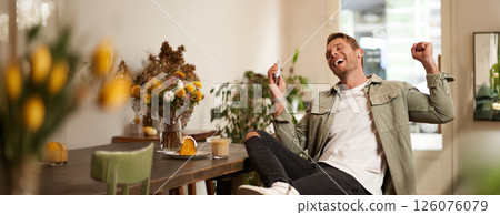 Portrait of handsome happy man in cafe, listens to music in wireless earphones, holding smartphone, connects to public wifi and enjoys favourite song, relaxing in coffee shop 126076079