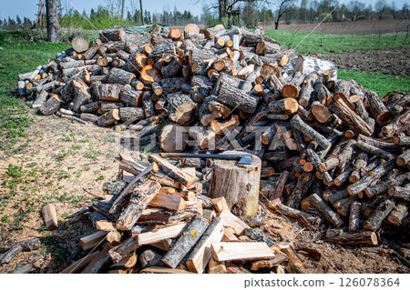 Pile of Firewood Logs Stacked in Rural Yard with Split Wood in Foreground 126078364