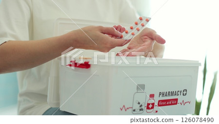 Woman takes out blister of pills from first aid kit at home. 126078490
