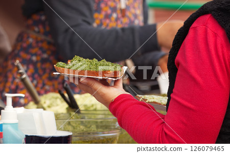 Close-Up of Hand Holding a Pesto-Topped Bread at Street Food Market 126079465