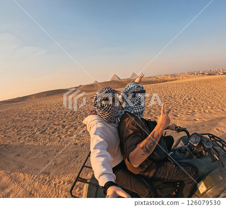 Tourists riding quad bike near giza pyramids at sunset, making peace sign 126079530