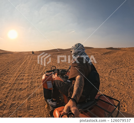 Tourist riding quad bike exploring desert landscape at sunset Tourist riding quad bike exploring desert landscape at sunset 126079537