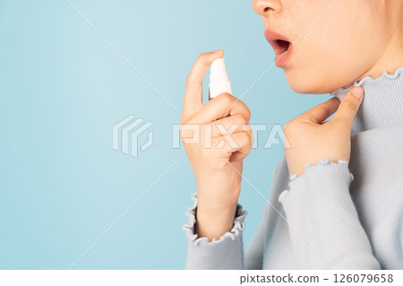 Sick woman using spray medication for relief of painful sore throats, cough, pharyngitis and hoarseness on light blue background. Pharmaceutical product. Health care and medical concept. Close up. 126079658