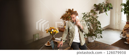 Portrait of happy young manager, man having negotiations, business conversation over the phone, talking on mobile, sitting in office on table with laptop 126079938