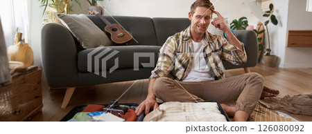 Portrait of worried man, tourist looking stressed and concerned, packing suitcase, holding hands on head, deciding on what to bring on holiday Portrait of worried man, tourist looking stressed and concerned, packing suitcase, holding hands on head, deciding on what to bring on holiday 126080092