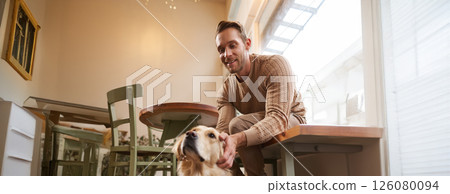 Vertical shot of young smiling man with his dog, golden retriever pet in a cafe 126080094