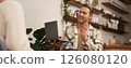 Portrait of young smiling man, coworker joins online meeting from cafe, video chats on laptop, shows okay, ok hand sign in approval, drinking coffee and working remotely 126080120