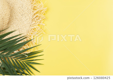 Vacation travel planning simple theme of straw hat and palm leaves on uniform yellow background flat lay with copy-space 126080425