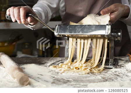 Caucasian female hands making fettuccine noodles using mechanical pasta machine 126080525