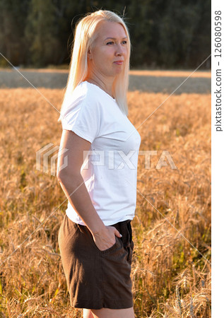 Woman stands in a golden field of wheat during sunset, showcasing natural beauty and serenity in a rural setting Woman stands in a golden field of wheat during sunset, showcasing natural beauty and serenity in a rural setting 126080598