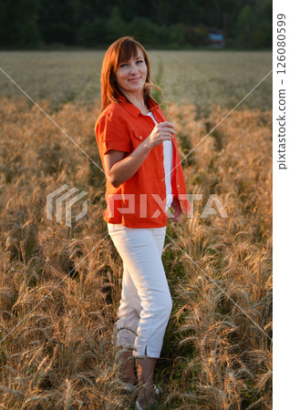 Woman with long hair in pink dress stands in golden wheat field during sunset, highlighting natural beauty and serene landscape Woman with long hair in pink dress stands in golden wheat field during sunset, highlighting natural beauty and serene landscape 126080599