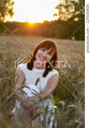 Woman with long hair in pink dress stands in golden wheat field during sunset, highlighting natural beauty and serene landscape Woman with long hair in pink dress stands in golden wheat field during sunset, highlighting natural beauty and serene landscape 126080600