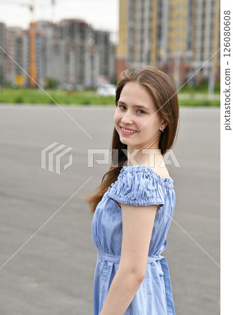 Smiling young woman in blue top looking at the camera outdoors on a blurred city background. 126080608