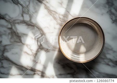 Shallow ceramic bowl on a marble surface with sunlight casting intricate shadows around it 126080774