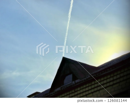 thin plane trail in blue sky above triangular roof, geometric shape in sunlight thin plane trail in blue sky above triangular roof, geometric shape in sunlight 126081144